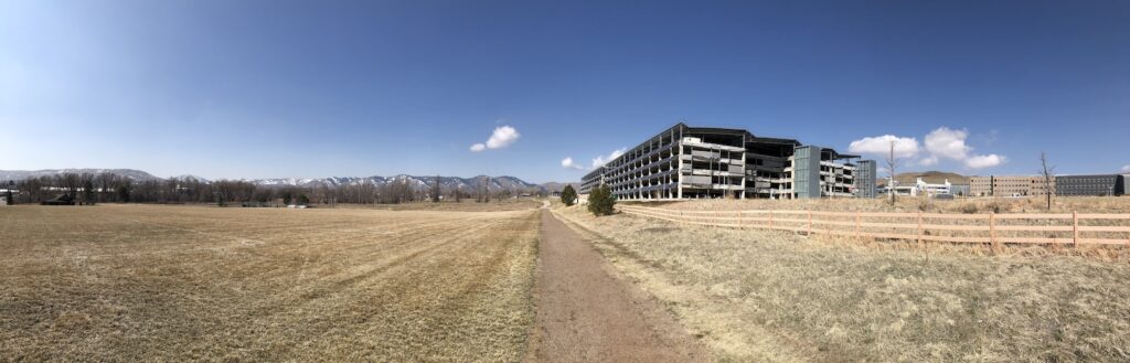 Panoramic view of the landscape near the NREL Laboratory. Most of the image is grassy fields, the Rocky Mountains are in the background, the garage looms in the middle right of the image.
