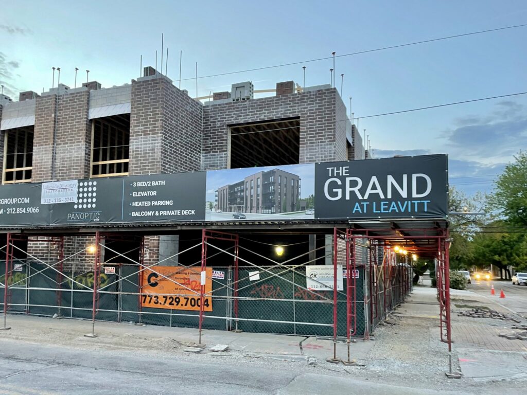 Photo of The Grand at Leavitt, a housing project under construction with signs boasting "heated parking" among other amenities.